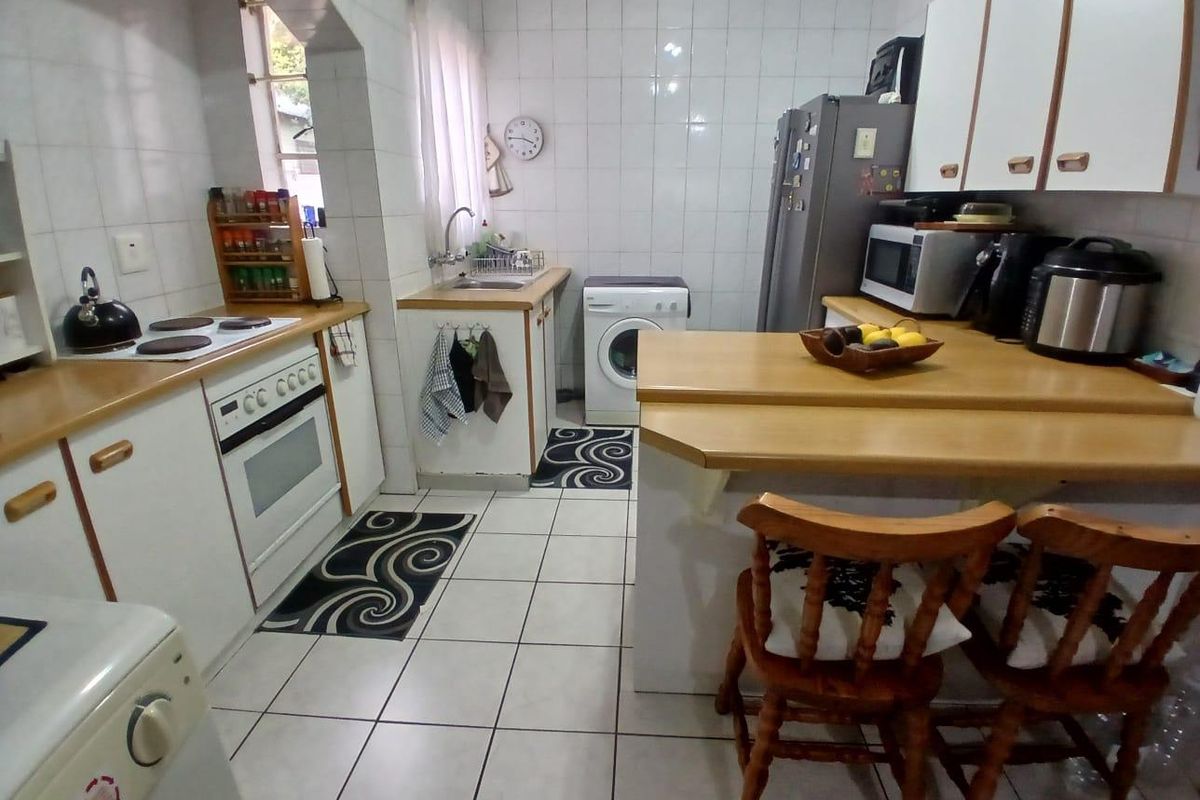 Functional kitchen featuring built-in cabinetry, integrated oven and hob, tiled splashbacks, and a breakfast bar counter.