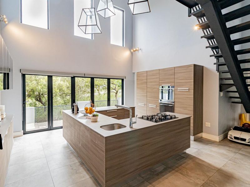 Modern open-plan kitchen featuring a central island with gas cooktop, sleek cabinetry, double-height ceilings, and large windows overlooking the garden.