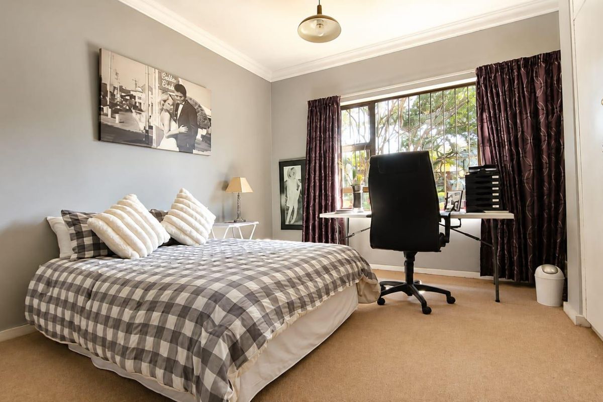 A bedroom featuring neutral wall tones, carpeted flooring, a built-in wardrobe, and a window with security bars overlooking the exterior.