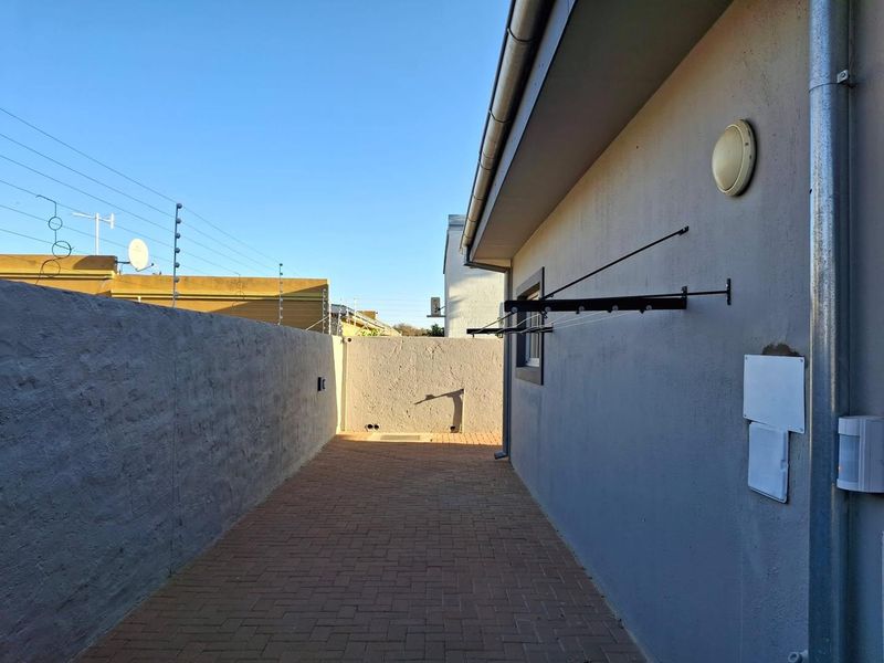 A paved side passage or rear exterior area featuring a boundary wall with electric fencing and a wall-mounted clothesline.