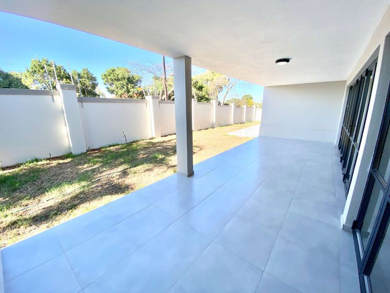 A spacious, modern covered patio featuring large format floor tiles, a structural support column, and direct access to the garden area.