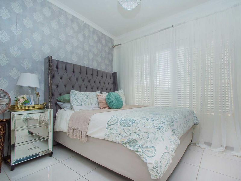 A well-maintained bedroom featuring tiled flooring, decorative wallpaper, and window blinds, offering a clean and comfortable living space.