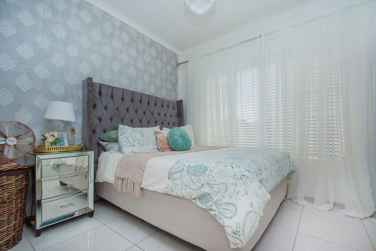 A well-maintained bedroom featuring tiled flooring, decorative wallpaper, and window blinds, offering a clean and comfortable living space.