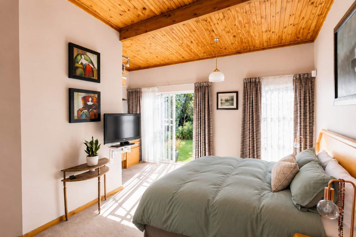 A bright bedroom featuring a vaulted timber-clad ceiling, carpeted flooring, and sliding glass doors providing direct access to the garden.