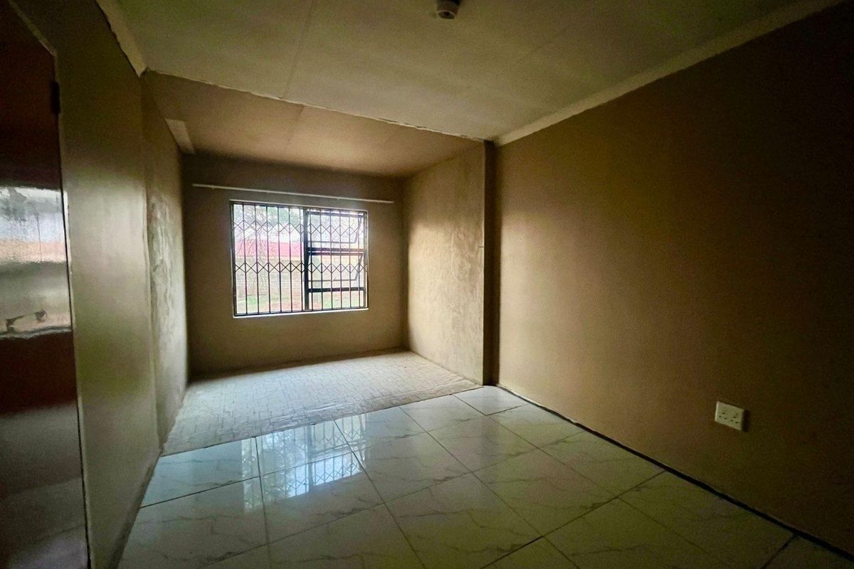 An empty bedroom featuring tiled flooring and security bars on the window, currently requiring finishing work on the walls and ceiling.
