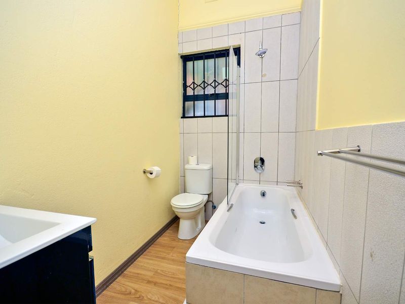 A functional bathroom featuring a bathtub with shower attachment, toilet, and vanity basin, finished with yellow painted walls and tiled wet areas.