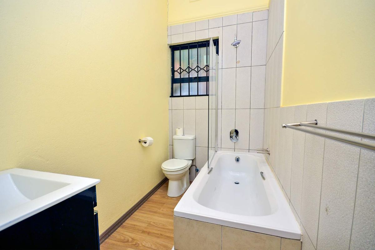 A functional bathroom featuring a bathtub with shower attachment, toilet, and vanity basin, finished with yellow painted walls and tiled wet areas.