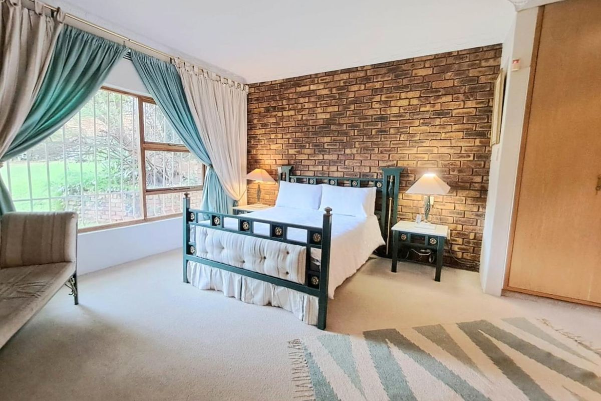 A bedroom featuring a prominent exposed brick feature wall, built-in wooden cabinetry, and large windows overlooking the garden.