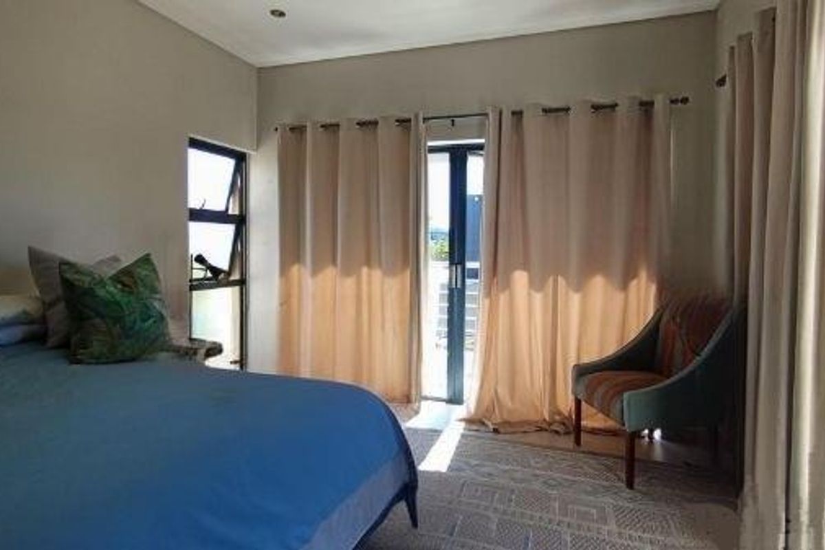 A well-lit bedroom featuring large windows and a glass door leading to an outdoor area, providing natural light and access to the exterior.