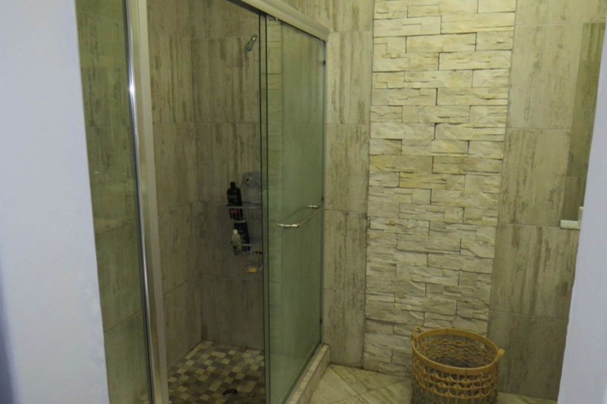 A modern bathroom featuring a glass-enclosed shower with textured stone wall cladding and neutral floor tiling.