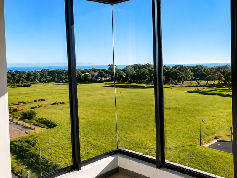 A bright, modern corner space featuring expansive floor-to-ceiling windows offering panoramic views of the surrounding green landscape and distant ocean.