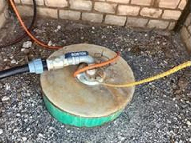 A functional borehole pump installation with associated water piping and electrical connections located against a brick wall.