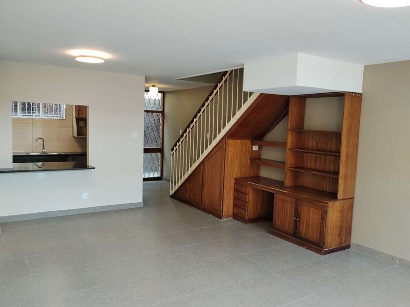 Open plan living area featuring tiled floors, a built-in staircase with integrated storage cabinetry, and a convenient pass-through window to the kitchen.