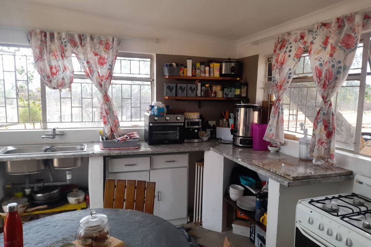A functional kitchen area featuring granite countertops, built-in cabinetry, a gas stove, and double stainless steel sink with large windows overlooking the garden.