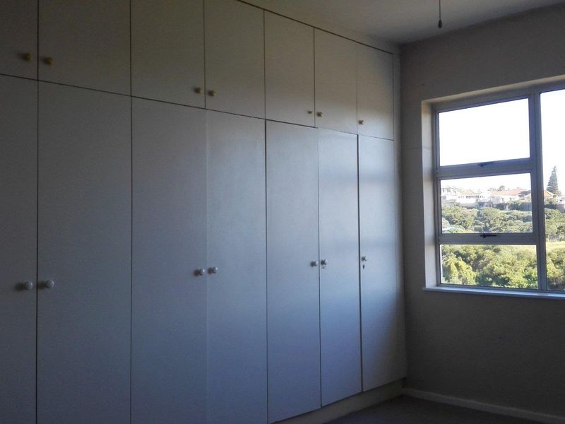 A bedroom featuring extensive floor-to-ceiling built-in cupboards and a large window with natural light and exterior views.