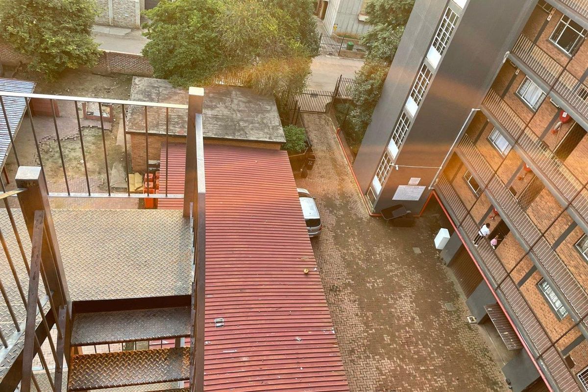 An elevated aerial view of the apartment complex grounds, featuring a metal staircase, paved courtyard area, and surrounding building facades.
