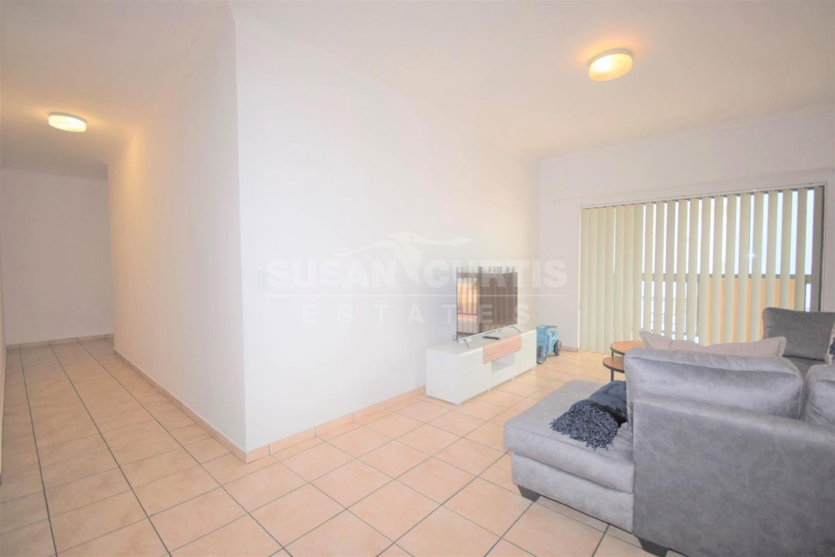 A living room area featuring tiled flooring, vertical blinds, and neutral wall finishes, providing a functional and bright living space.