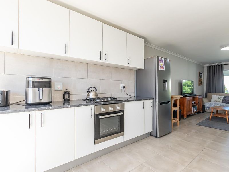 Modern open-plan kitchen featuring white cabinetry, stone-look countertops, and integrated gas hob and oven, flowing seamlessly into the adjacent living area.