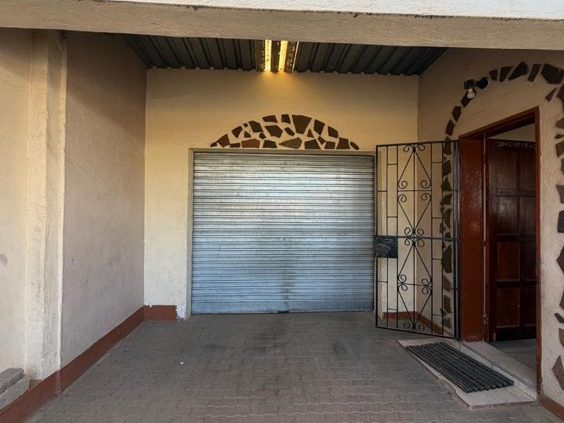 A covered garage area featuring a roller shutter door, security gate, and paved flooring with decorative stone cladding accents.