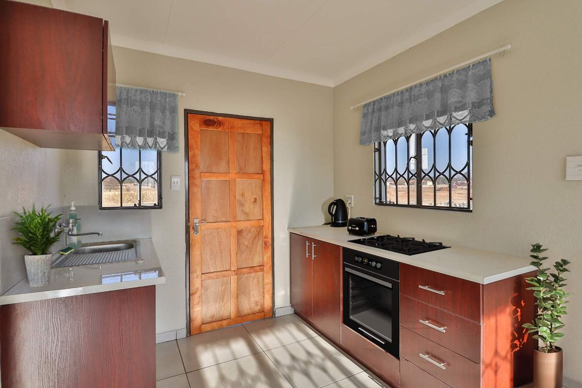 A functional kitchen featuring dark wood cabinetry, a built-in oven, gas hob, stainless steel sink, and tiled flooring with security bars on the windows.