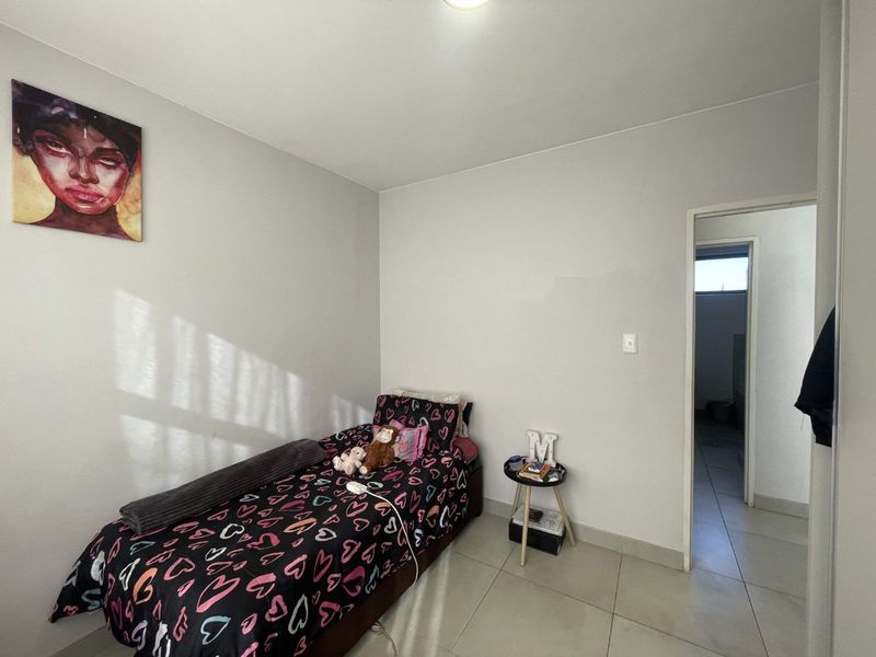 A functional bedroom featuring neutral wall finishes and tiled flooring, providing a clean and simple space with direct access to an adjoining room.