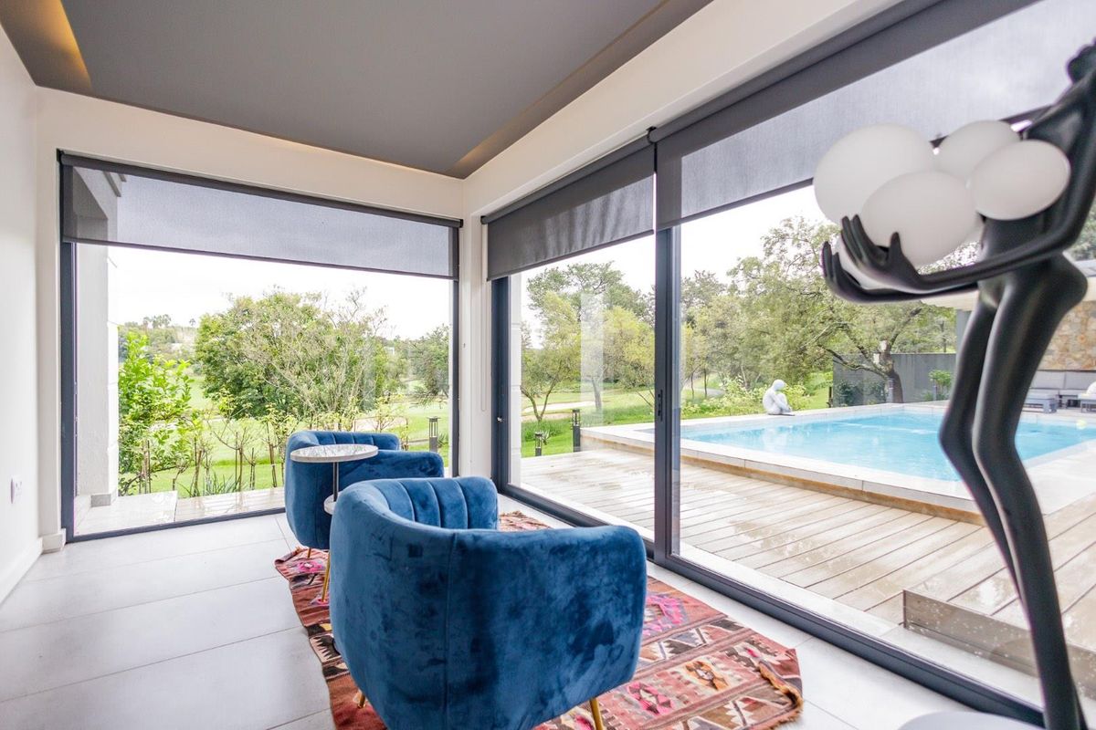 Bright living area featuring floor-to-ceiling sliding glass doors that open onto a wooden deck and swimming pool with scenic garden views.