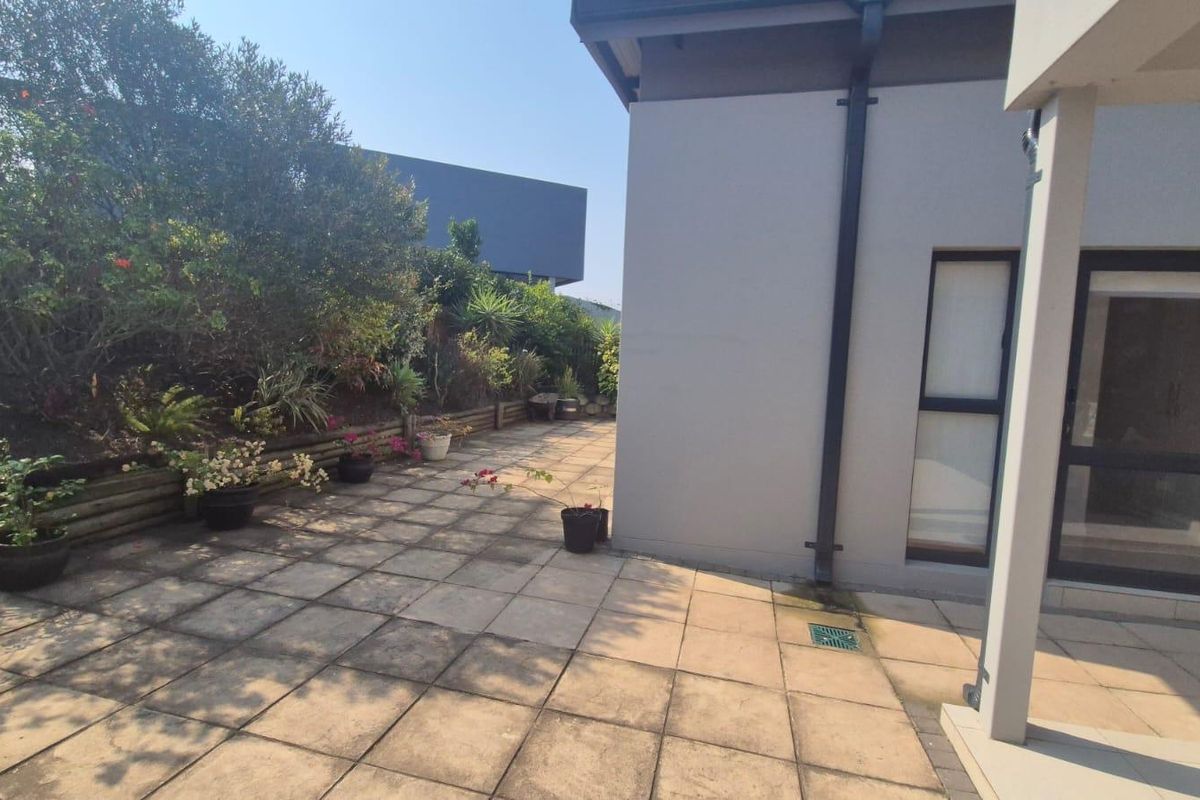 A paved rear patio area featuring a retaining wall, drainage system, and direct access to the home's exterior.