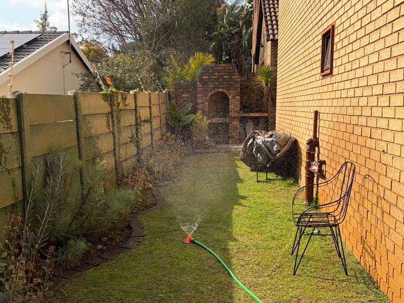 A side garden area featuring a built-in brick braai, brick exterior wall, and precast boundary fencing with solar panels visible on the roof.