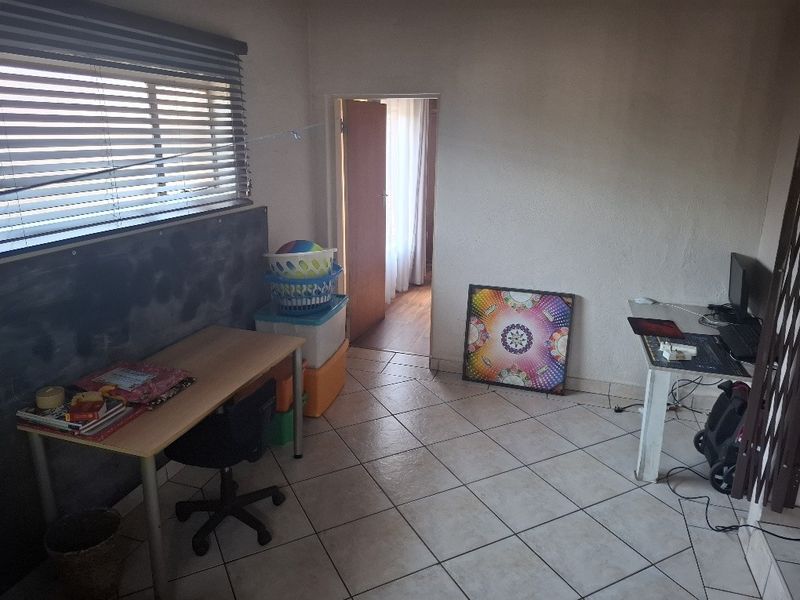 A bedroom featuring tiled flooring and venetian blinds, currently utilized as a workspace with visible wear on the wall surfaces.