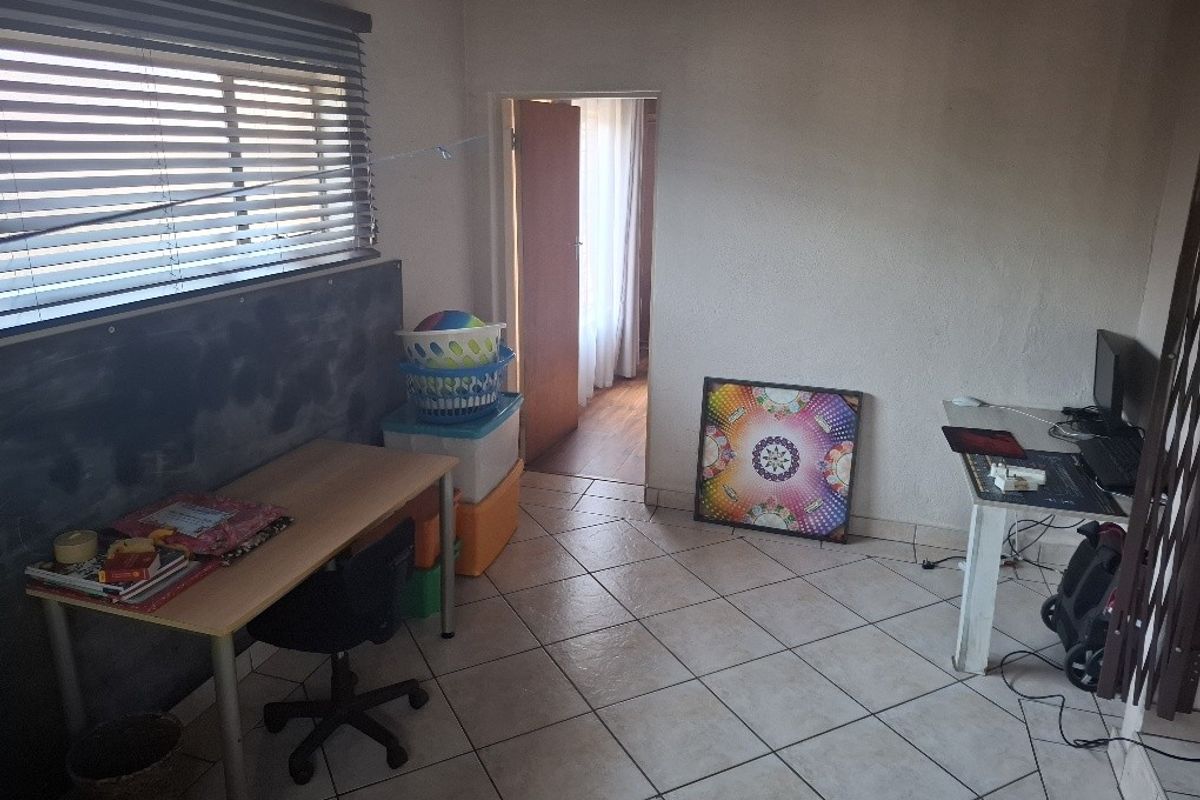 A bedroom featuring tiled flooring and venetian blinds, currently utilized as a workspace with visible wear on the wall surfaces.