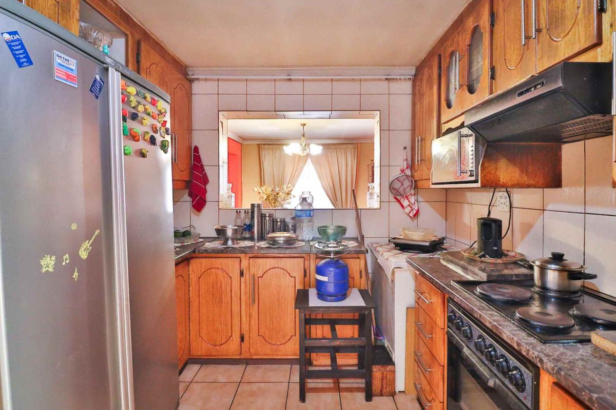 A functional kitchen featuring wooden cabinetry, tiled backsplash, and a serving hatch that opens into the adjacent living area.