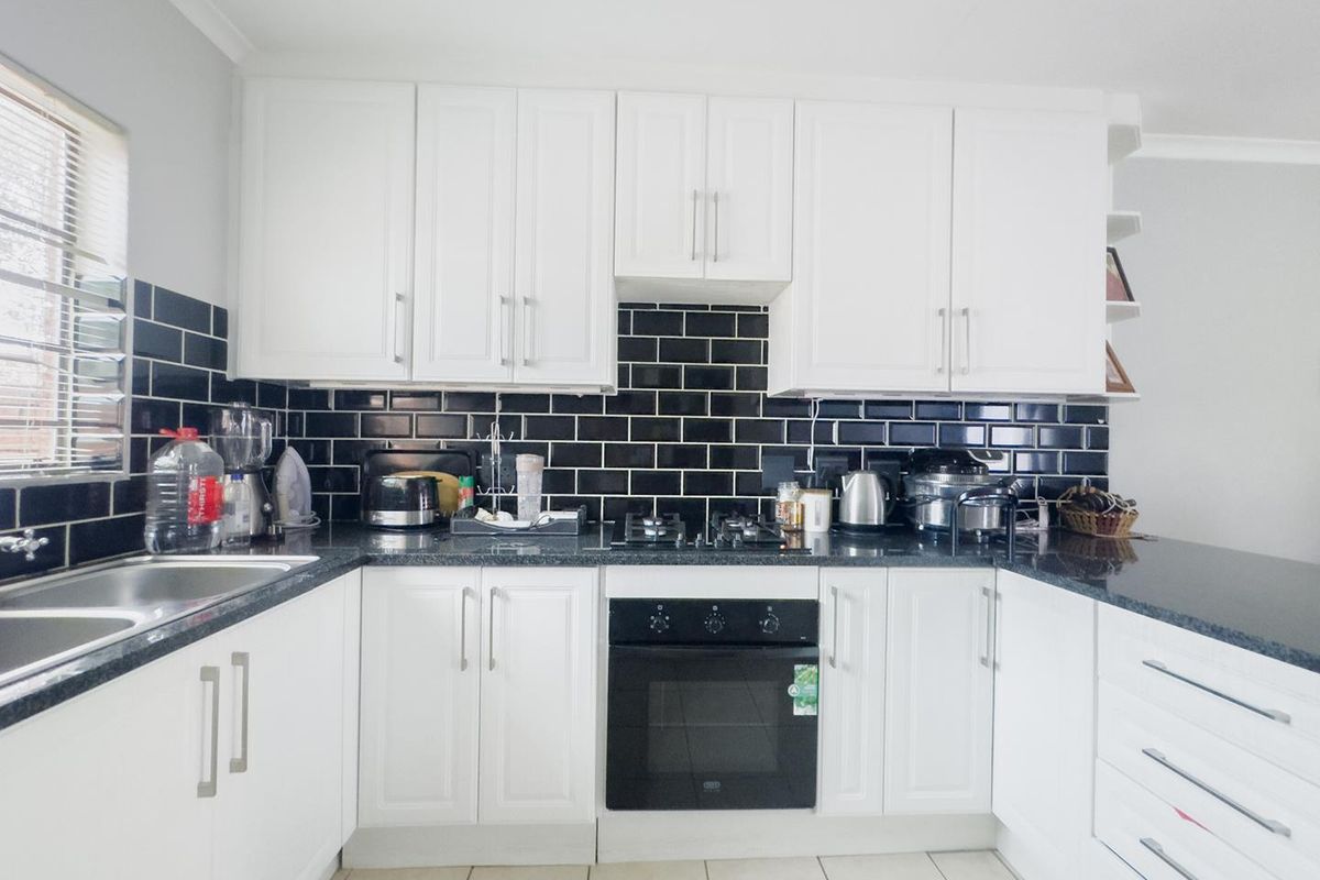 A well-maintained kitchen featuring white cabinetry, contrasting black subway tile backsplash, granite countertops, and integrated stainless steel appliances.