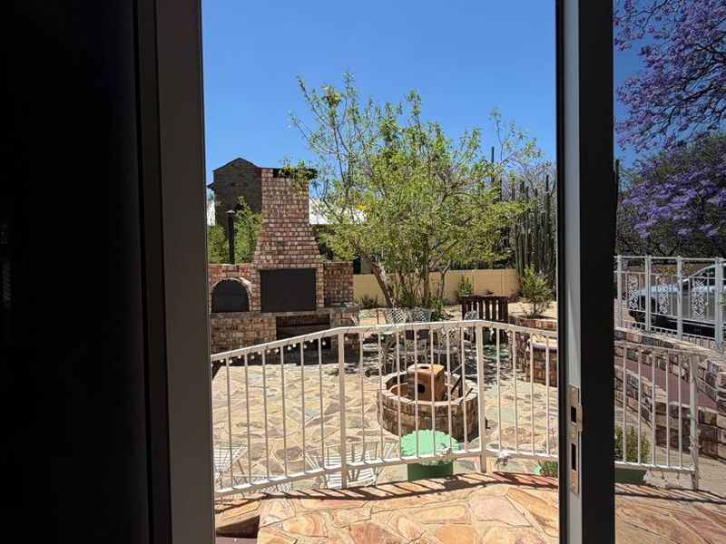 View from an interior doorway looking out onto a paved patio area featuring a built-in brick braai and metal safety railing.