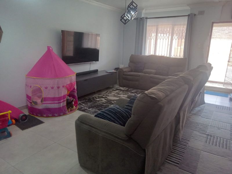 A comfortable living room featuring tiled flooring, modern lighting, and a security gate leading to the exterior.