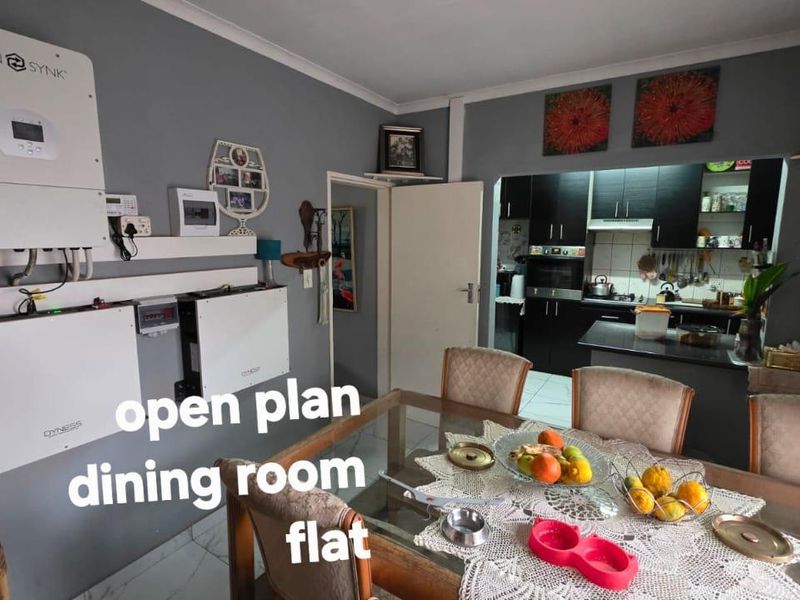 Open plan dining area featuring a wall-mounted solar power system and an adjacent kitchen with dark cabinetry and built-in appliances.