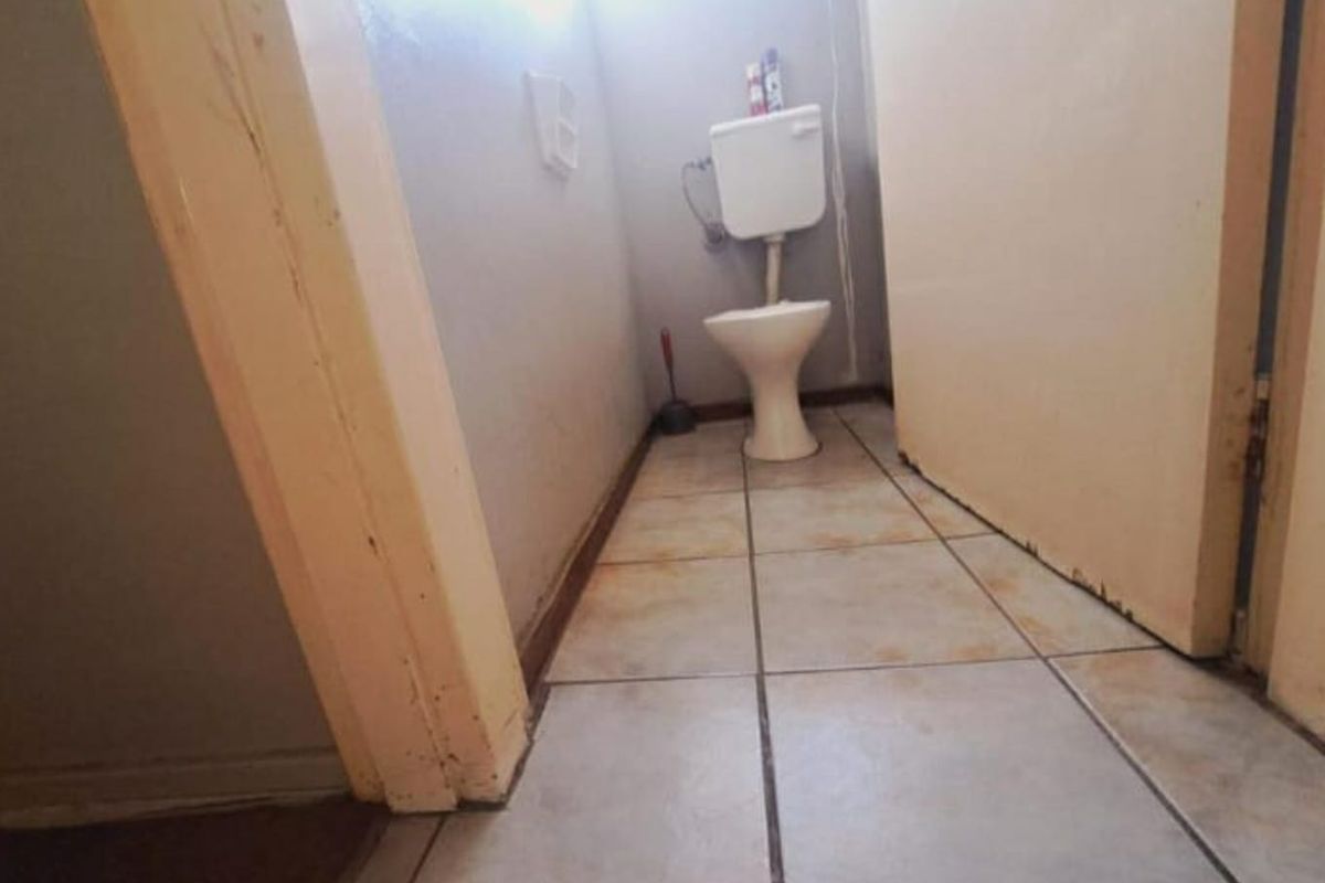 A small bathroom featuring a standard toilet suite and tiled flooring, currently showing significant signs of wear and requiring maintenance or renovation.