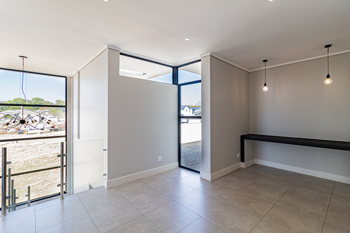Modern, light-filled living space featuring large format floor tiles, sleek black aluminium window frames, a glass balustrade, and contemporary pendant lighting.