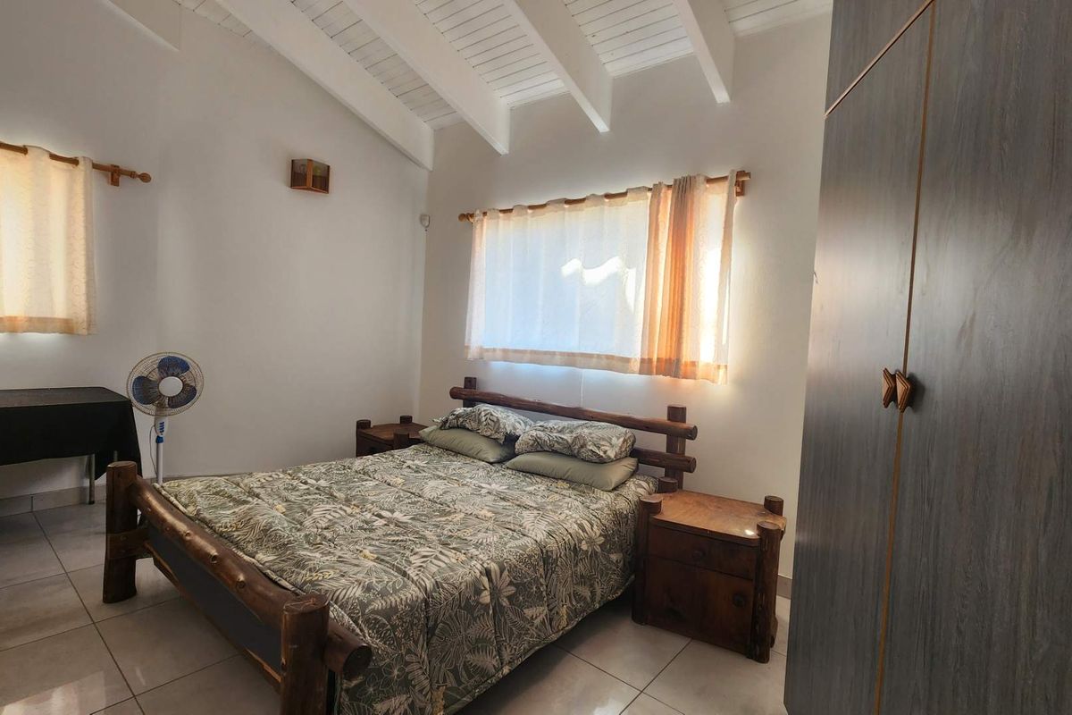 A bedroom featuring exposed timber ceiling beams, tiled flooring, and a built-in wardrobe, offering a functional space with natural light.