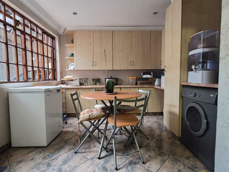 A functional kitchen featuring laminate cabinetry, tiled flooring, and a large timber-framed window, providing a practical space for meal preparation and casual dining.