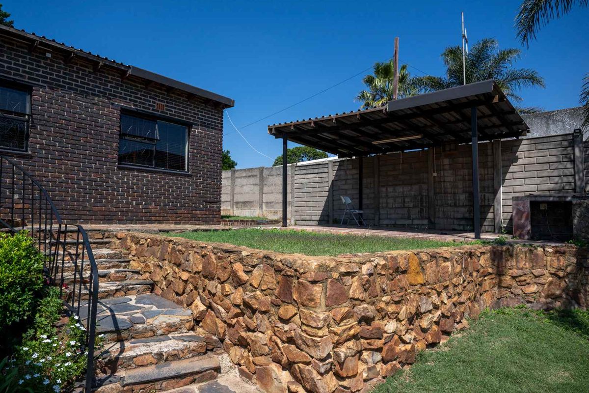 Rear garden area featuring a stone retaining wall, slate staircase with iron railing, and a covered patio structure with a concrete block boundary wall.