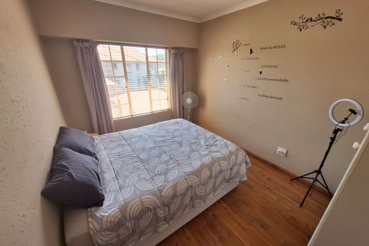 A bedroom featuring wooden flooring, a large window with blinds, and neutral wall finishes.
