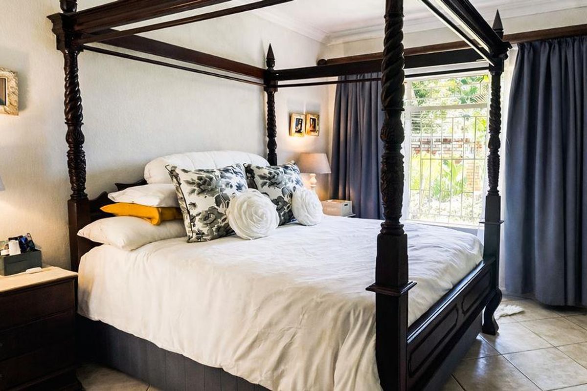 A well-lit bedroom featuring tiled flooring, a large window with security bars, and neutral wall finishes.