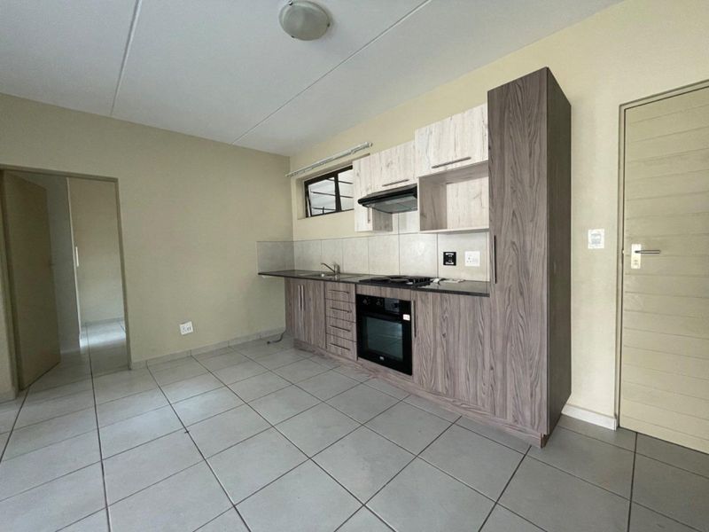 A clean, functional kitchen featuring modern wood-grain cabinetry, built-in oven and hob, tiled flooring, and a neutral backsplash.
