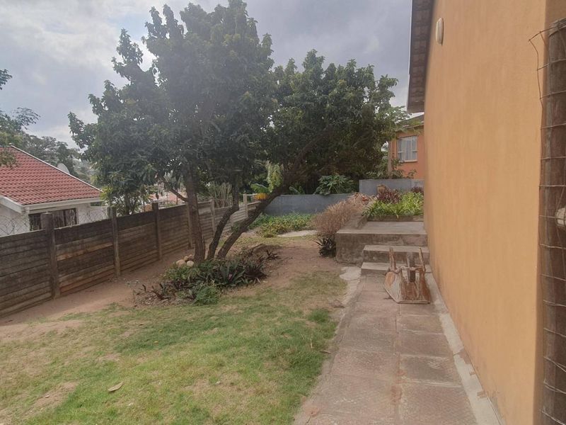 A view of the rear garden area featuring a concrete pathway, steps, and perimeter fencing with established trees.
