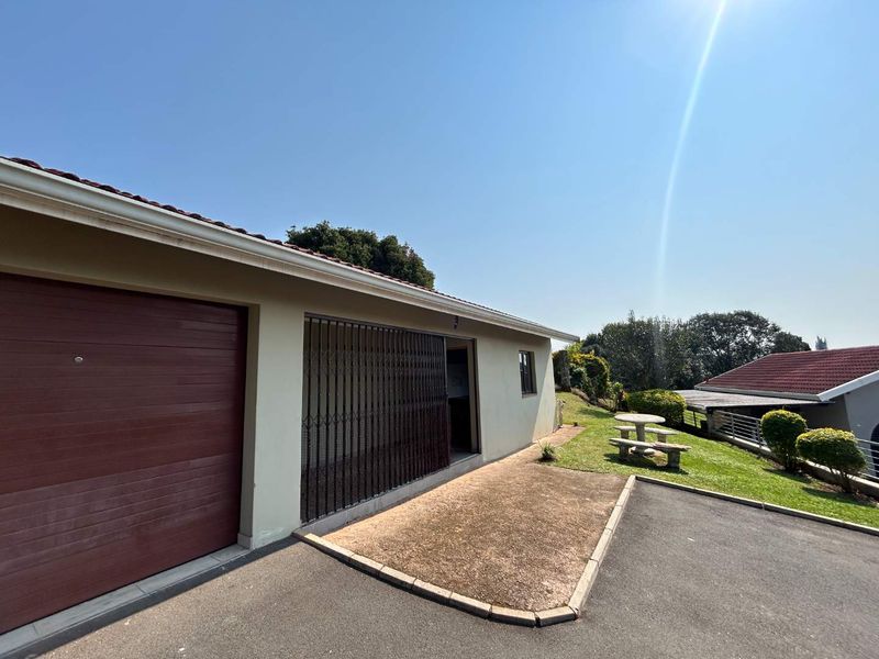 Exterior view of the cottage featuring a garage, security gate entrance, and paved driveway area with surrounding garden space.