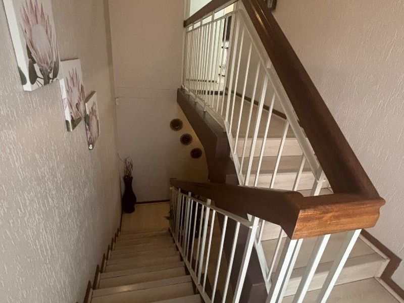 A staircase featuring a wooden handrail and metal balustrade, connecting different levels of the townhouse with a textured wall finish.