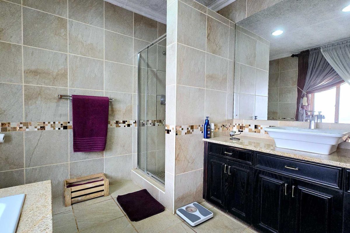 A well-appointed bathroom featuring a glass-enclosed shower, a modern vessel sink on a dark wood vanity, and neutral floor-to-ceiling wall tiles.