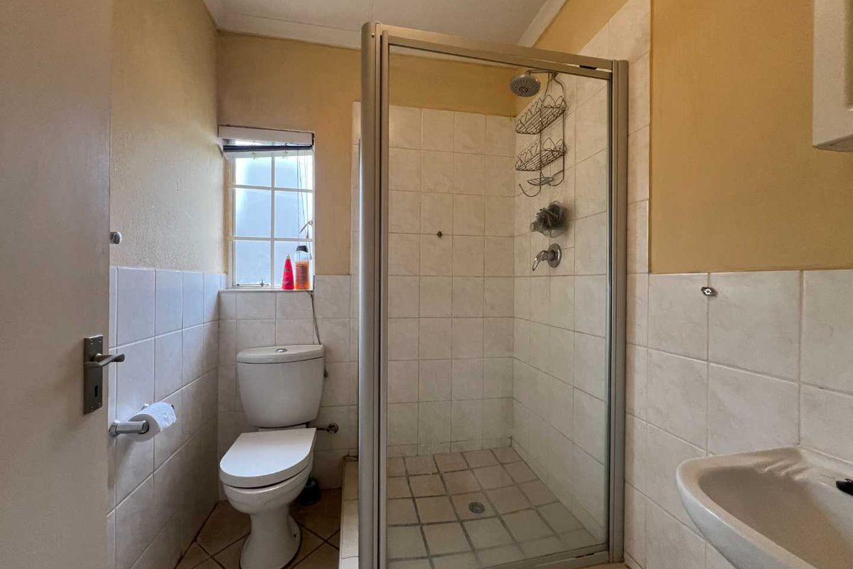 A compact bathroom featuring a glass-enclosed shower, a standard toilet, and a wall-mounted basin with tiled walls and flooring.