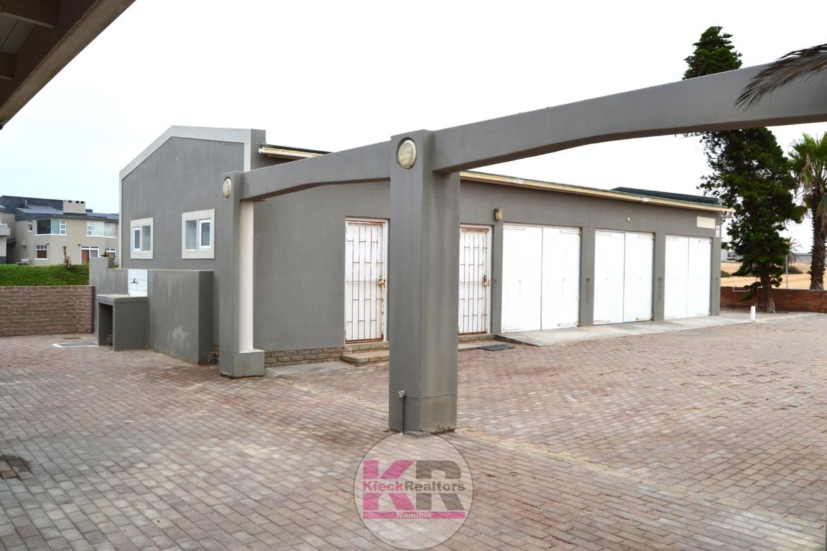 Rear exterior view featuring a triple garage, paved driveway, and an outdoor wash basin area with structural archway.