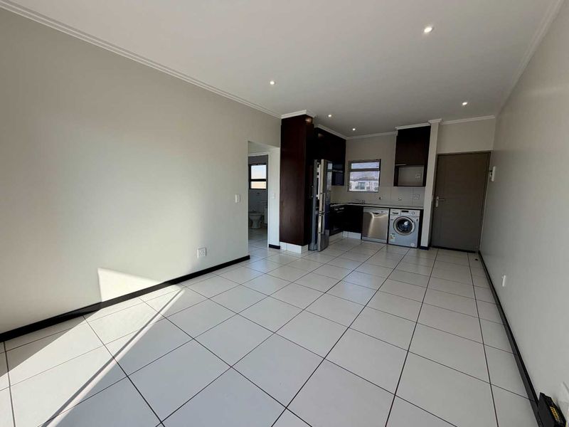 An open-plan living and kitchen area featuring tiled flooring, recessed lighting, and modern built-in cabinetry with integrated appliances.